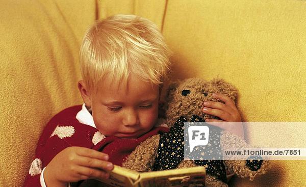 Boy lesen ein Buch beim Spielen mit ein Teddybär