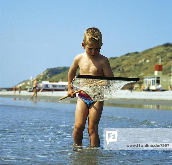 Junge mit Fischnetz im Wasser am Strand  Niederlande