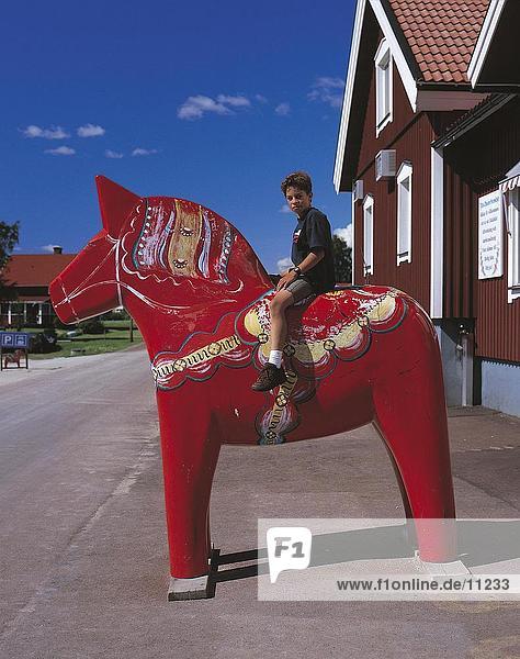 Side profile of boy sitting on wooden red horse  Dalarna  Sweden