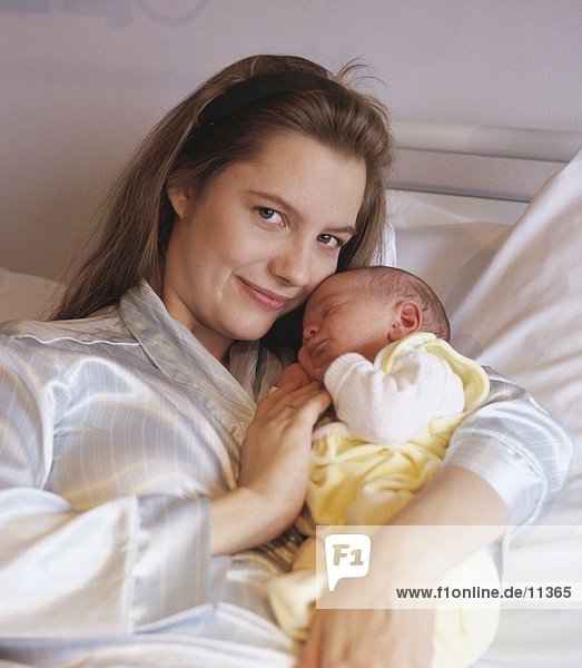 Portrait einer jungen Frau mit ihr neugeborenes Baby auf Bett