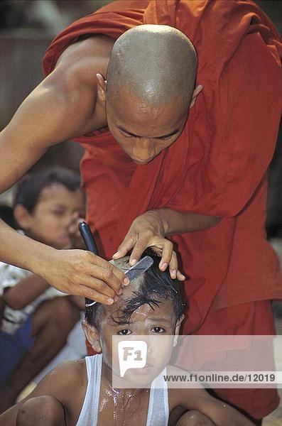 Buddhist monk shaving head of boy  Shin Byu Festival  Myanmar