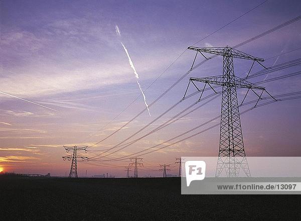 Electricity pylons in field at sunset