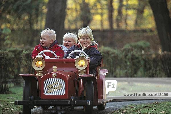 Drei Kinder Reisen in ein Spielzeugauto auf ein Bahngleis