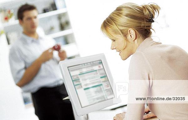 Side profile of a young woman working on a computer with a young man standing in the background
