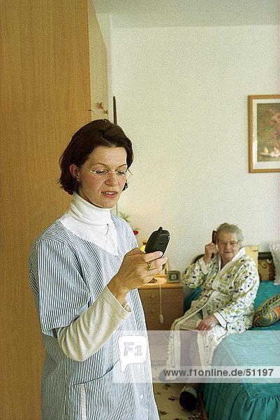 Krankenschwester mit Handy mit Patienten im Hintergrund