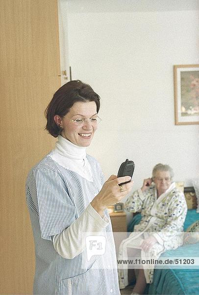 Krankenschwester mit Handy mit Patienten im Hintergrund