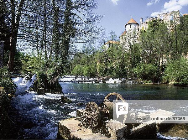Broken Wassermühle in einem Fluss mit einer Burg im Hintergrund Slowenien