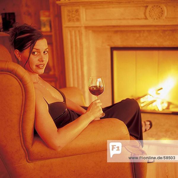 Junge Frau im Sessel sitzen und halten ein Glas Wein