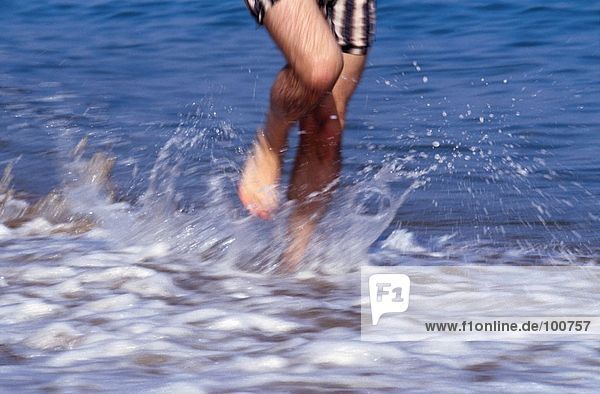 Low section view of man running in water on beach