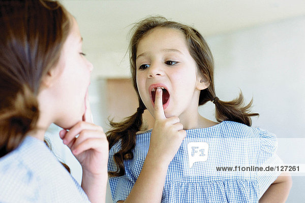 Mädchen schaut auf ihren fehlenden Zahn im Spiegel