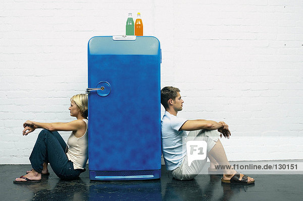 Couple seated against a fridge