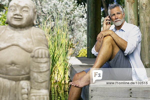 Mann neben Pool und Buddha mit Handy