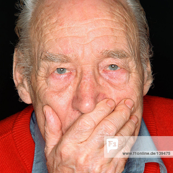 Ein älterer Mann  der seinen Mund mit der Hand bedeckt.