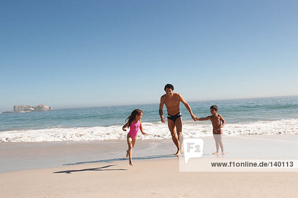 Vater und Kinder  die am Strand rennen