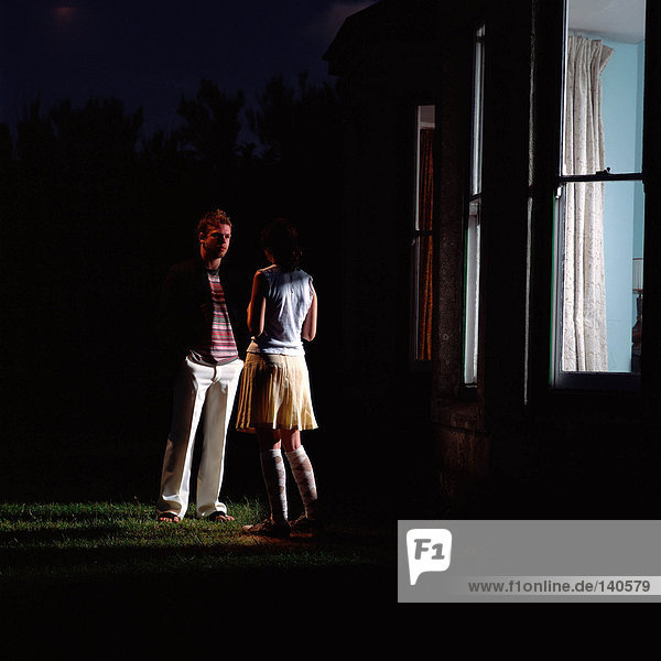 Junges Paar steht vor einem Haus im Dunkeln