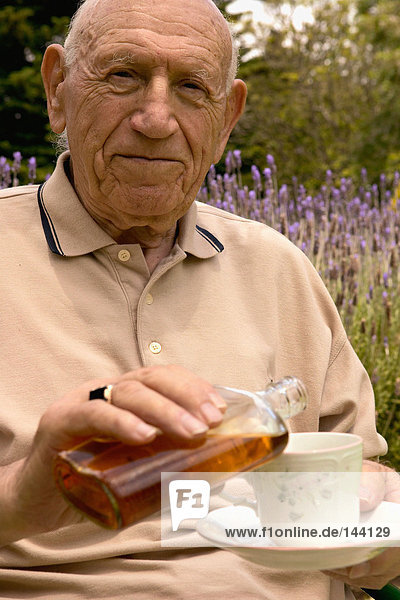 Ein älterer Mann  der Alkohol in seine Teetasse gießt.