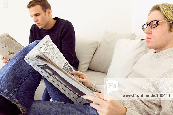 Men reading newspapers on sofa