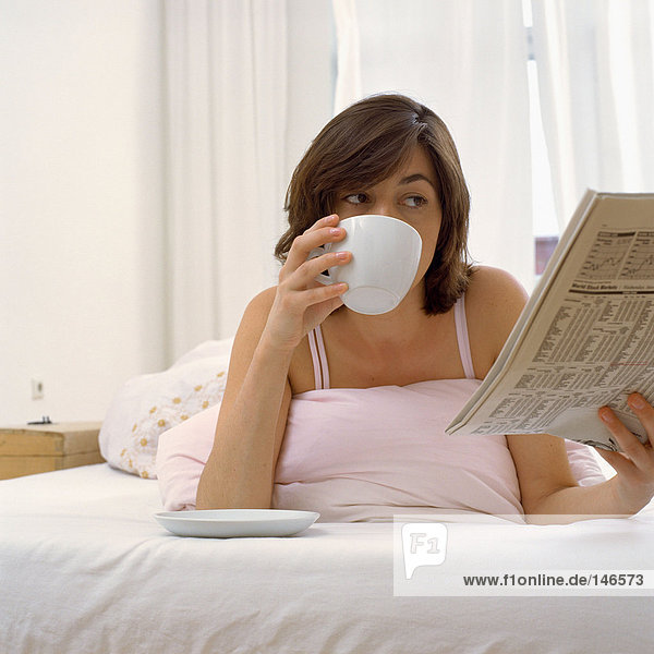 Woman in bed with tea & paper