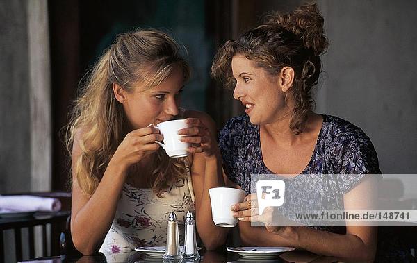 Two young women holding cups of coffee in sidewalk cafe