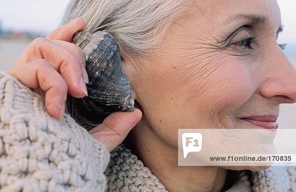 Seniorin hält sich eine Muschel ans Ohr