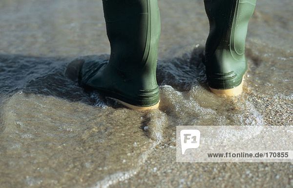 Person in Gummistiefeln im Meer stehend