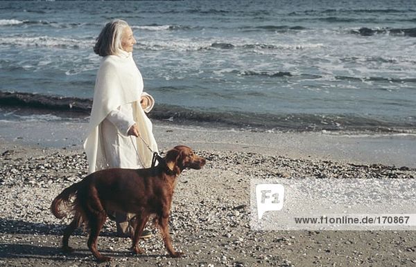 Senior woman walking dog by the sea