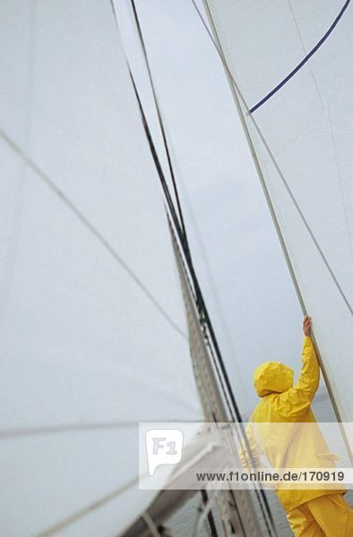 Person on boat in yellow waterproofs leaning on sail