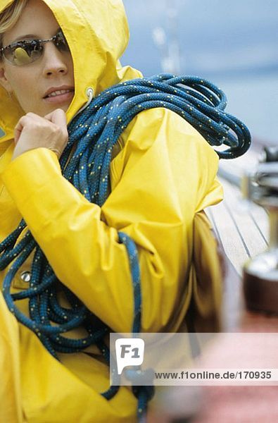 Woman in yellow raincoat and sunglasses carrying rope