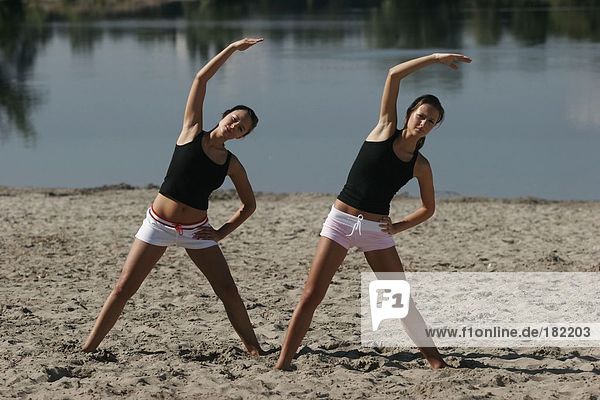 Two young women doing fitness exercises at beach  full shot