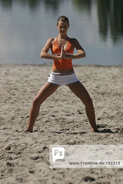 Portrait of young woman doing yoga on lake beach