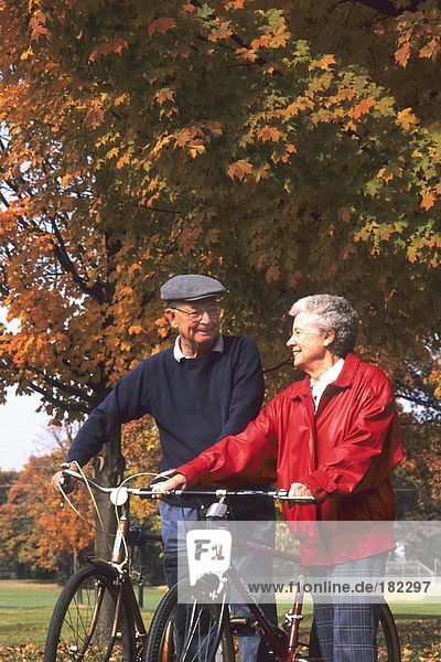 älteres Paar mit Fahrrädern im Park spazieren