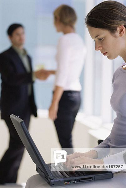 Woman using laptop as colleagues shake hands