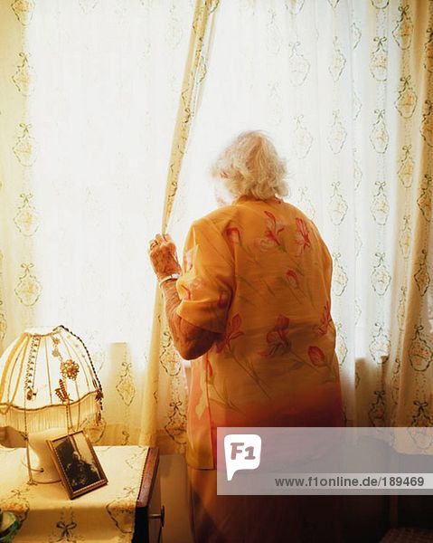 Ältere Frau  die den Vorhang öffnet.