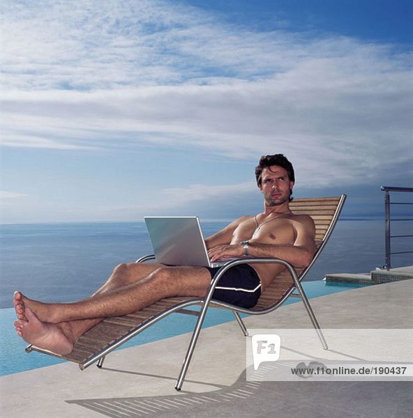 Mann mit Laptop am Pool