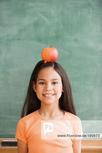 Schulmädchen  das einen Apfel auf dem Kopf balanciert.