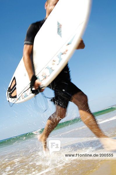 Mann mit Surfboard am Strand
