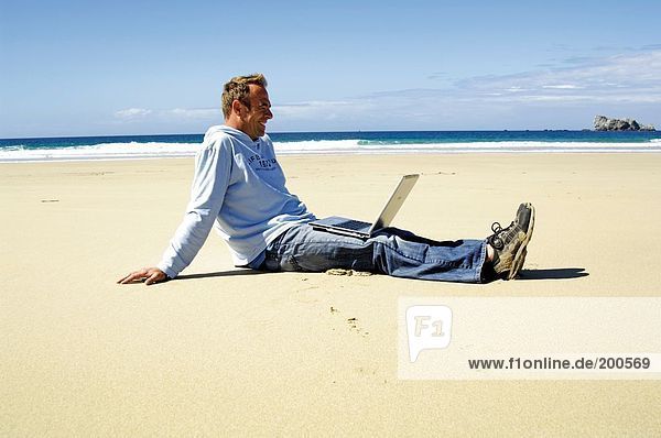 Side profile of man sitting with laptop on beach