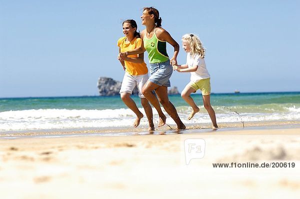 Woman running with her two daughters on beach