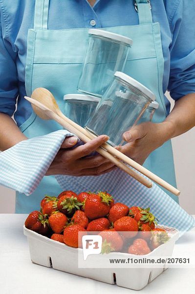 Frau mit Einmachgläsern  Kochlöffeln und Schale Erdbeeren