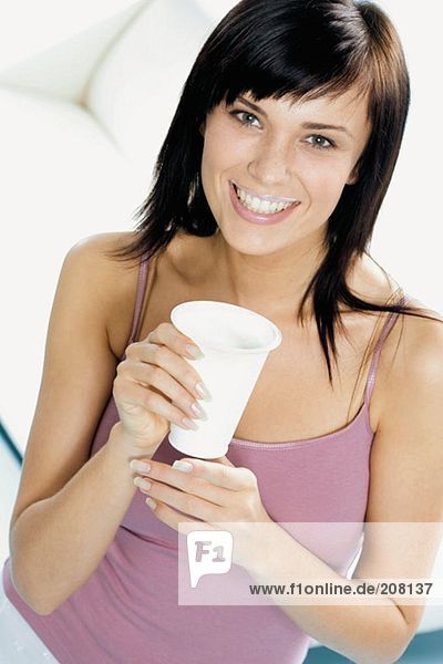 Junge Frau mit einem Becher Trinkjoghurt und 'Milchbart'