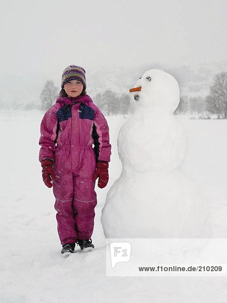 Girl standing next to snowman