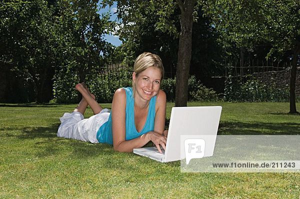 Frau auf dem Rasen liegend mit Laptop