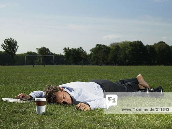Männlicher Büroangestellter schläft in einem Park
