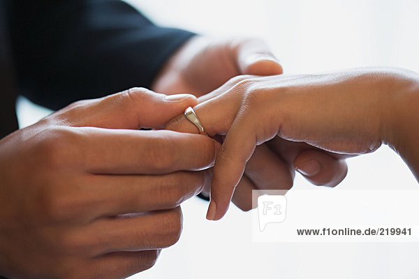 Bräutigam platziert Ehering auf Bräute Finger