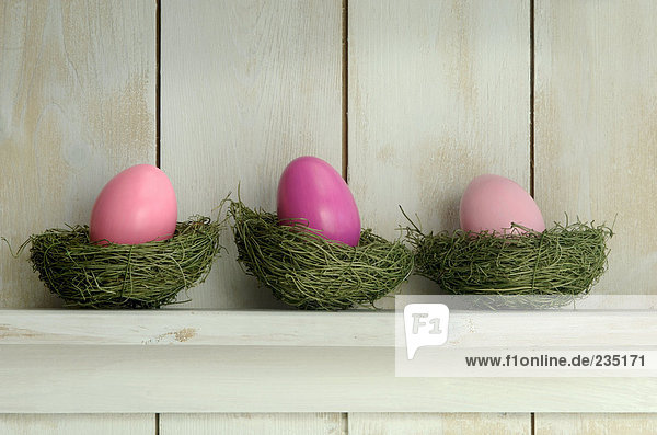Pink Easter eggs in nest on wooden shelf