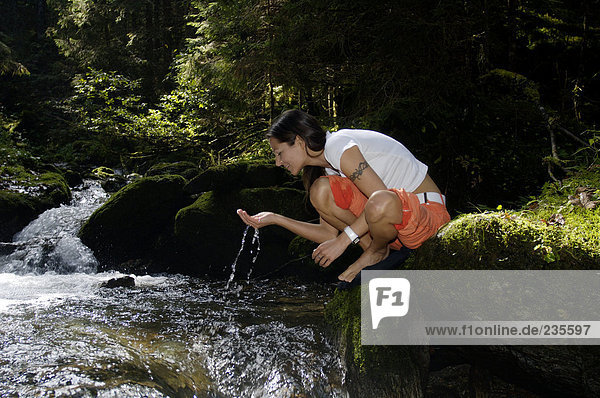 Österreich  Frau trinkt Wasser aus einem Bach im Wald