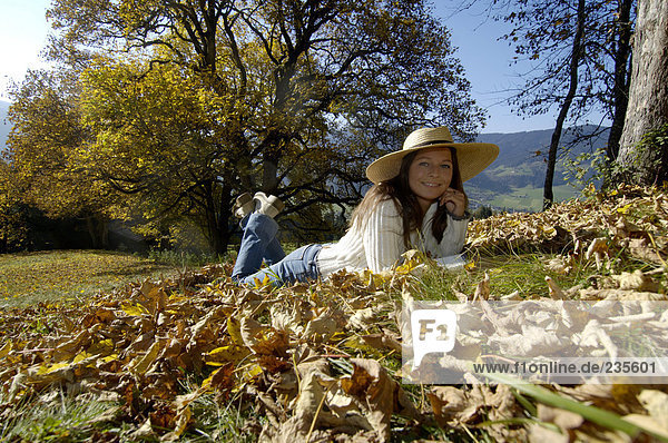 Junge Frau auf Herbstlaub liegend mit Hand am Kinn  Portrait