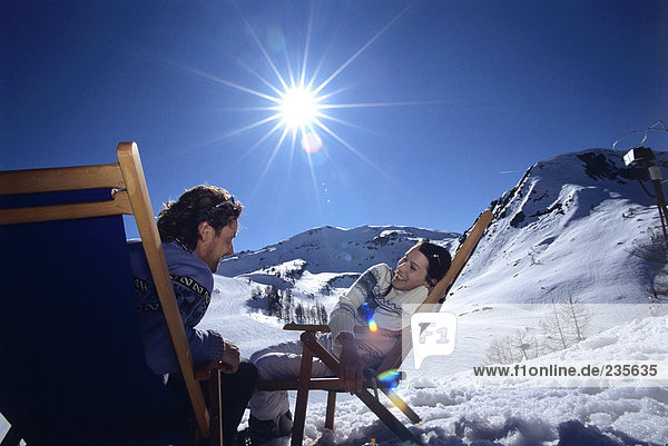 Junges Paar auf Liegestühlen in den Alpen sitzend  lächelnd