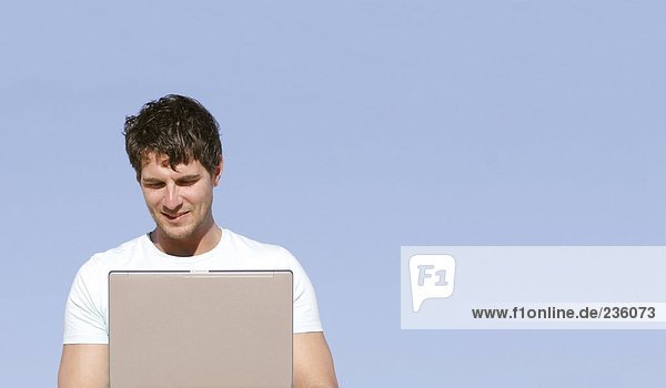 Mann im Freien sitzend mit Laptop  lächelnd