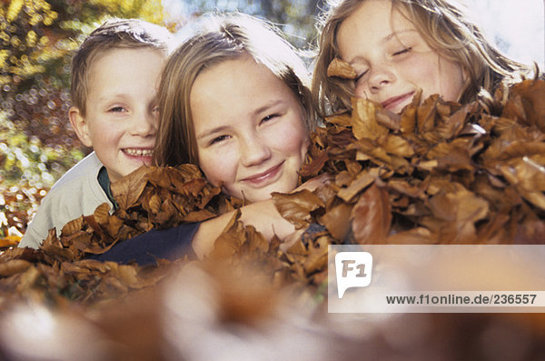 Kinder (4-13) auf Herbstblättern liegend